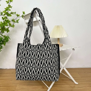 Knitted tote bag with black and white wave pattern hanging on a white folding chair