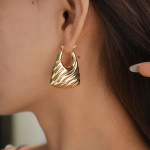 Macro detail of golden geometric earrings with textured wave surface on model's ear