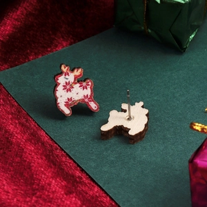 Macro view of Christmas reindeer stud earrings with red snowflake pattern on white wood