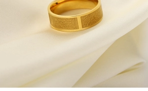 Close-up of golden stainless steel ring with textured rectangular patterns on silk cloth