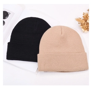 Flat lay of black and beige knit beanies with magazine and dried flowers on white background