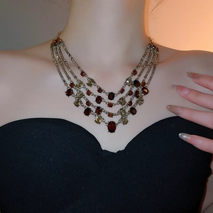 Close-up of layered gold tassel necklace with vintage red and green gemstones on a model