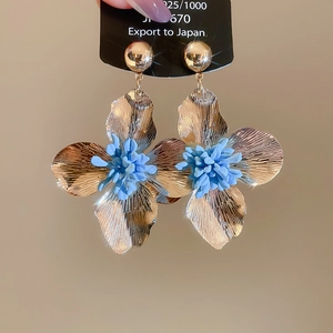 Detail of gold floral earrings with blue stamen and textured petals held on a black tag