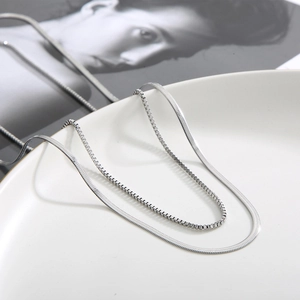 Detail of silver double-layered snake and box chain necklaces on white ceramic plate
