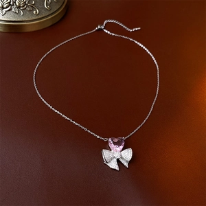 Détail du collier avec pendentif cœur rose en zircon et nœud sur un support vintage