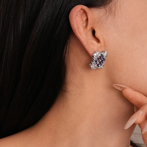 Detail of luxury geometric earrings featuring a purple square zircon on the earlobe