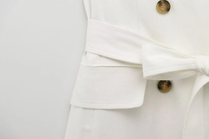 Detail of white blazer dress featuring brown buttons and adjustable bow-tie waist belt