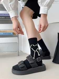 Dettaglio di calze nere con cuore in corda bianca intrecciata e sandali con plateau retrò