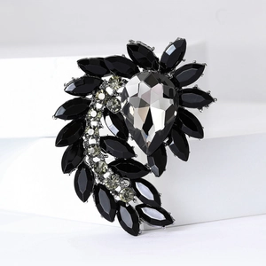 Macro shot of silver feather brooch featuring faceted black and grey crystals on white tiers