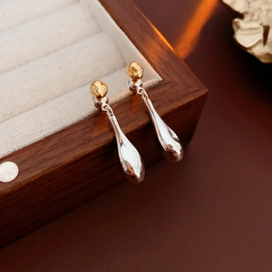 Macro shot of minimalist gold and silver teardrop earrings on a wooden jewelry display box