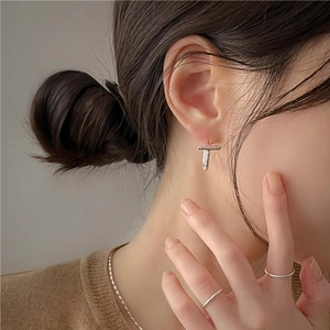 Macro view of minimalist silver T-shaped stud earring worn by model in elegant style