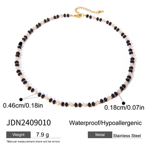 Detail of beaded necklace showing black beads, white faux pearls, and gold lobster clasp