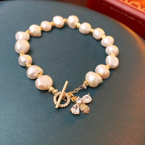 Detail of freshwater pearl bracelet with gold bee charm and T-bar clasp on green stone