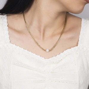 Detail of a gold Cuban chain necklace with white pearl worn by a female model