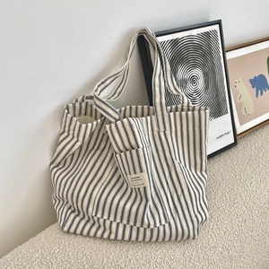 Detailed view of the striped canvas tote bag featuring an outer pocket and woven brand label