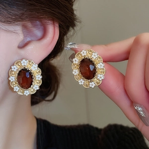 Close-up of vintage gold earrings with oval brown gemstone and white enamel floral details