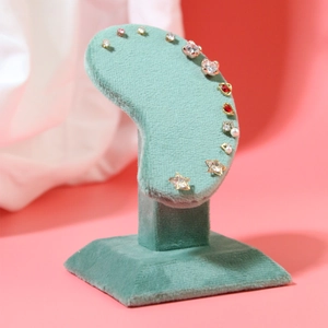 Green velvet ear-shaped jewelry stand displaying assorted stud earrings with cubic zirconia