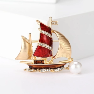 Detailed view of a gold sailboat brooch with red enamel, sparkling crystals, and a pearl