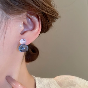 Close-up of translucent blue and white double bead stud earrings worn by a model