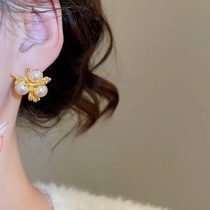Close-up of vintage gold branch stud earrings with white pearls worn by a model