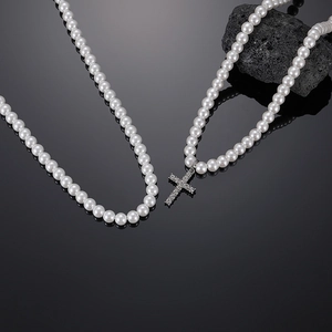 Close-up of pearl necklace featuring a diamond-encrusted cross pendant on dark rock