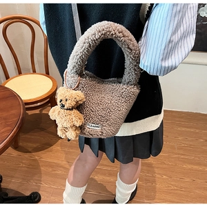 Détail du sac seau en peluche beige avec breloque ours dans un cadre intérieur chaleureux