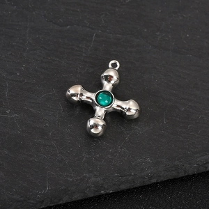 Detailed macro shot of a silver cross pendant featuring a centered green gemstone inlay