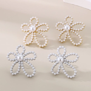 Detailed top view of pearl flower earrings in gold and silver finishes on beige surface