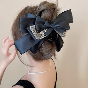 Detail of a large black satin bow hair claw with crystals on a bun from a back view