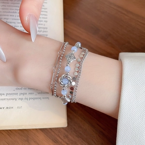 Detail of layered silver bracelets with blue beads and floral charms on a model wrist