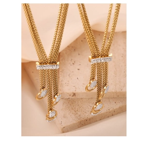 Detail of golden tassel sweater necklaces with rhinestones on beige stone background