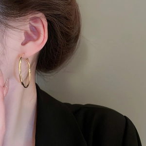 Close-up of a model wearing minimalist large gold hoop earrings with high-shine finish