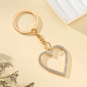 Golden heart-shaped keychain with sparkling rhinestones on a beige background with dried flowers