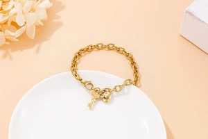 Detailed shot of a gold chunky chain bracelet with heart and key charms on a tray