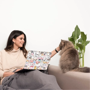 Cozy home scene of waterproof cartoon cat stickers applied on a laptop lid with a real cat