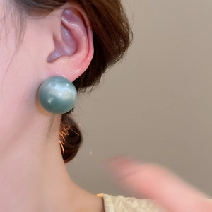 Close-up of elegant turquoise round stud earring worn on ear with pearl-like luster