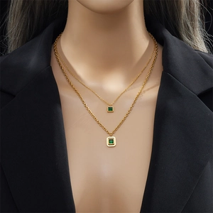 Detail view of double-layered gold plated necklace featuring two green square crystal pendants