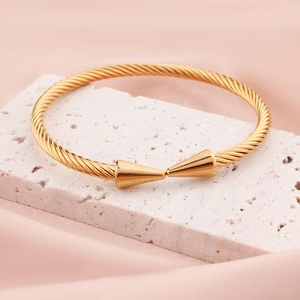 Gold titanium steel cable open bangle with spiked ends on a decorative stone base