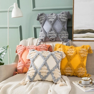 Close-up of tufted geometric cushion covers with tassels in multiple colors on sofa
