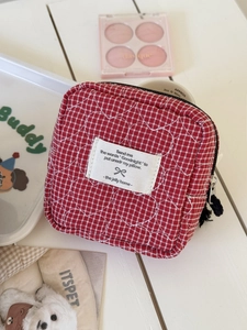 Red quilted heart pattern checkered storage bag for cosmetics on a white wooden table
