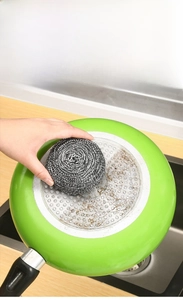Macro shot of a stainless steel scouring pad cleaning stubborn stains on a green frying pan
