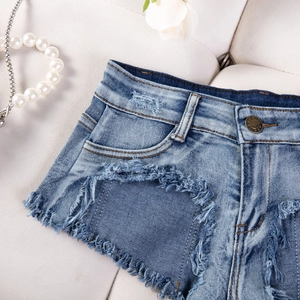 Dettaglio macro di pantaloncini di denim azzurro con forte usura e bordi grezzi sfilacciati