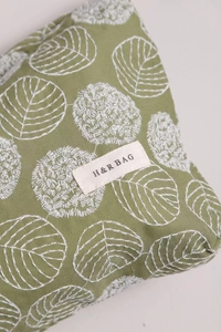 Detail of light green cotton linen pouch with delicate white flower embroidery and logo