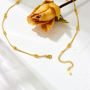 Golden stainless steel bead necklace with lobster clasp on a white textured background