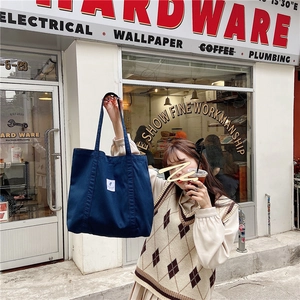Detail of dark blue corduroy tote bag with white label in an urban street setting