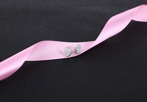 Macro shot of silver round stud earrings with white crystal pavé on pink ribbon