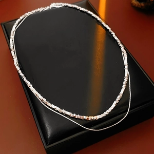 Detailed close-up of double-layer silver and rose gold chain necklace on black box