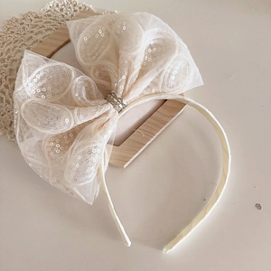 Détail d'un serre-tête beige avec nœud en tulle, broderie paillettes et texture tissée