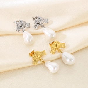 Detailed view of silver and gold bow-knot stud earrings with baroque pearl drops on silk