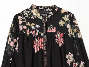 Détail du col d'un chemisier floral avec étiquette taille S sur tissu tissé noir